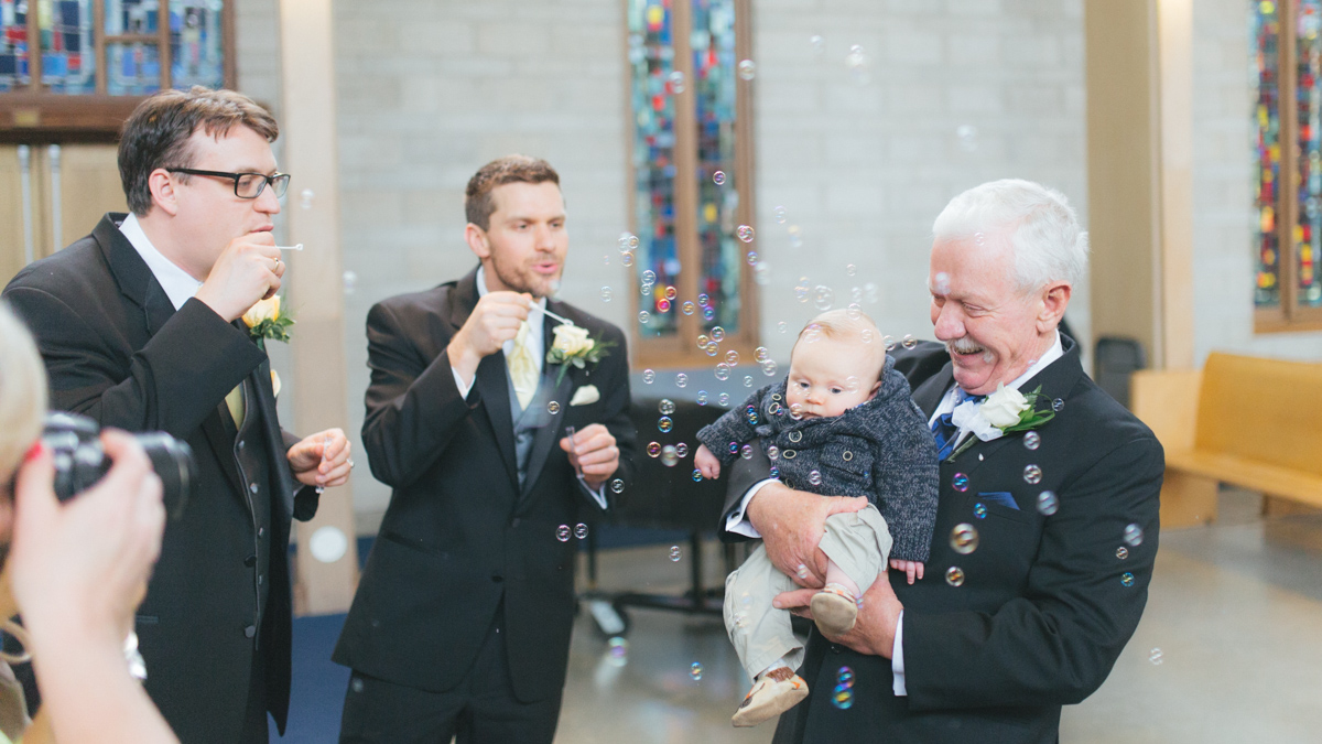 Father, baby and groomsmen having fun with bubbles after the ceremony